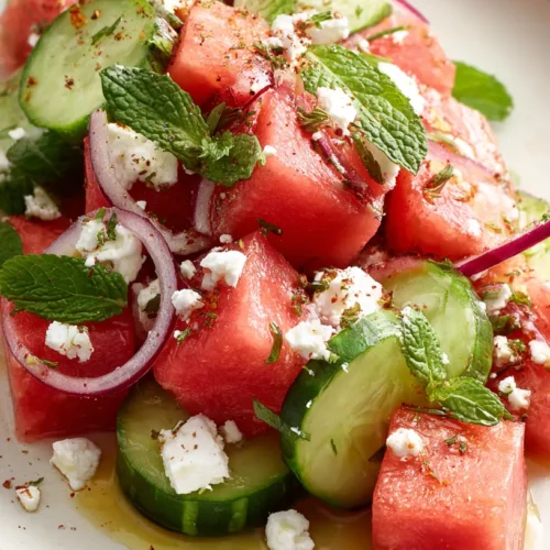 Close hero shot of watermelon cucumber salad with cucumber slices, watermelon cubes, feta, mint, and a dusting of sumac.