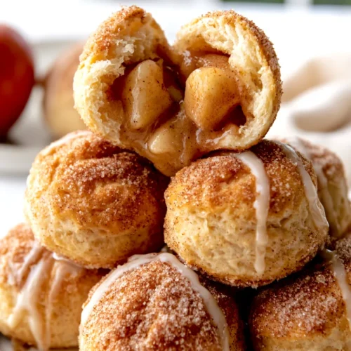 Hyper-realistic photo of golden air fryer apple pie bombs coated in cinnamon sugar, soft biscuit dough exterior with a slightly crisp golden finish, a few bobs split open to show warm gooey apple pie filling inside, light drizzle of vanilla glaze, served on a white ceramic plate, subtle cinnamon sugar scattered on the plate, bright white kitchen background, white marble countertop, cozy fall dessert styling, soft natural window light, crisp focus, realistic texture, editorial food photography, no text, no logos, no watermark, no people