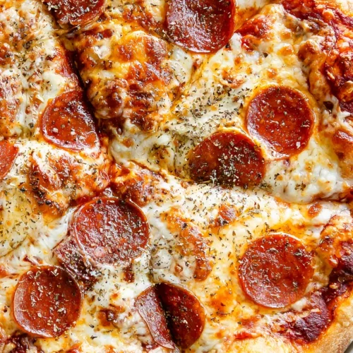 Homemade pizza, full whole pizza centered on a round white pizza pan, overhead angle, golden homemade crust with slightly blistered edges, bubbly melted mozzarella, rich red pizza sauce peeking through, scattered pepperoni slices and a light sprinkle of dried oregano, fresh-from-the-oven look, set on a white marble kitchen counter, bright white kitchen background, soft natural window light, hyper-realistic food photography, crisp textures, clean editorial styling, no people, no text, no watermark