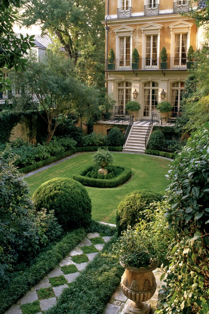 Formal Parisian courtyard garden with manicured boxwoods, stone pathway, and elegant ochre mansion with wrought-iron balconies