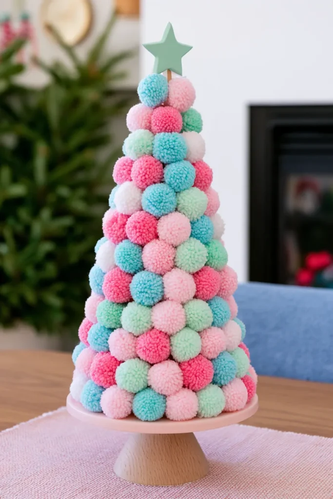 Colorful pom pom Christmas tree decoration in pastel pink, blue, green, and white, topped with a green star on a wooden pedestal